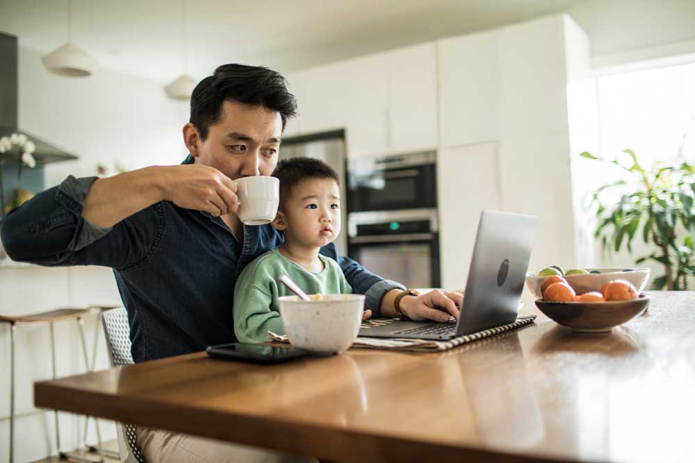 Man sitting with son at kitchen table drink coffee and reviewing computer