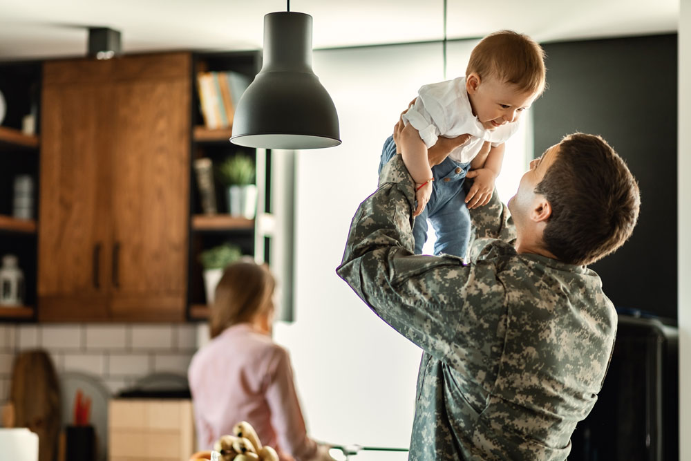 Military dad standing in the kitchen playing with his young son
