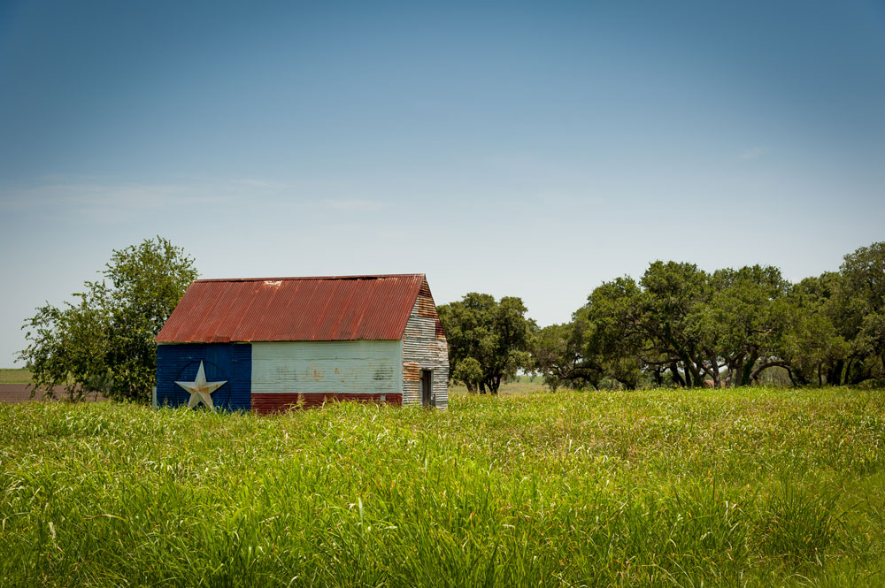 a barn in an open field with a Texas flag painted on the side