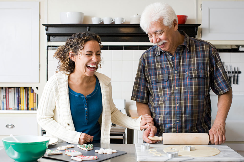 an older father and daughter laugh while baking together