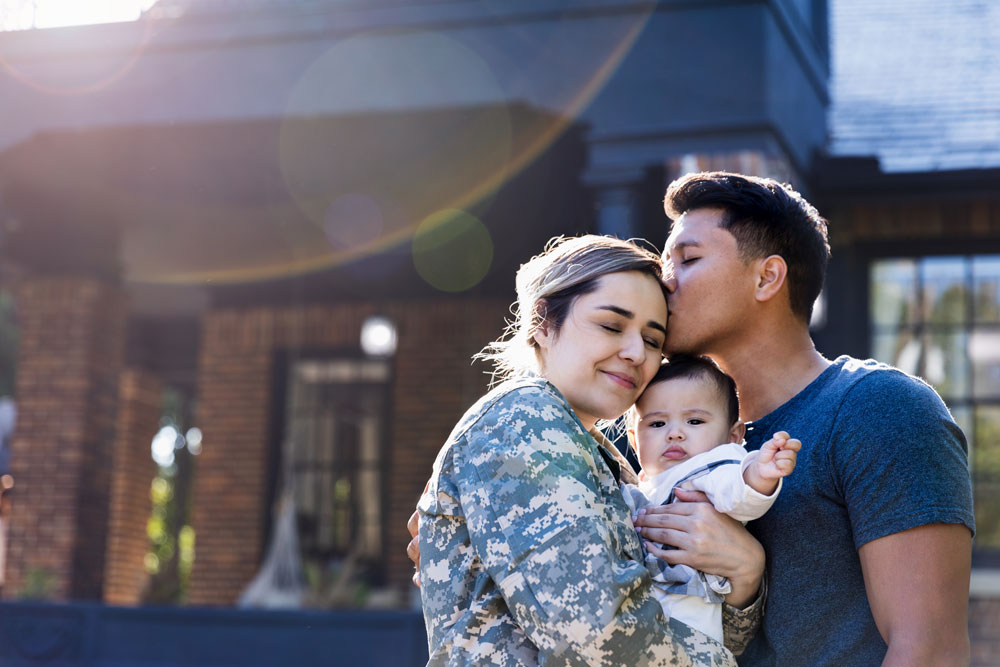 an active military woman hugs her family in front of their new home