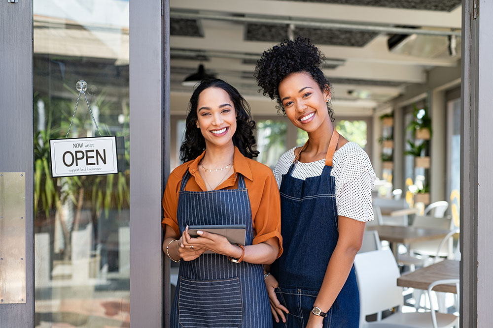 Ladies standing by their business besides a open now sign