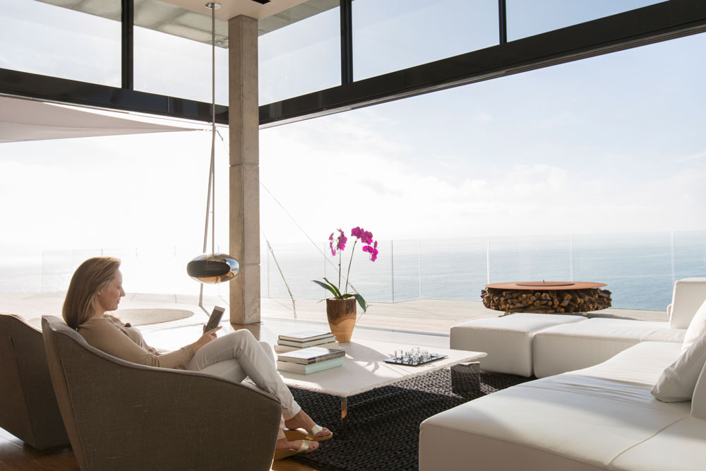 a woman sits reading a book in her house with an ocean view