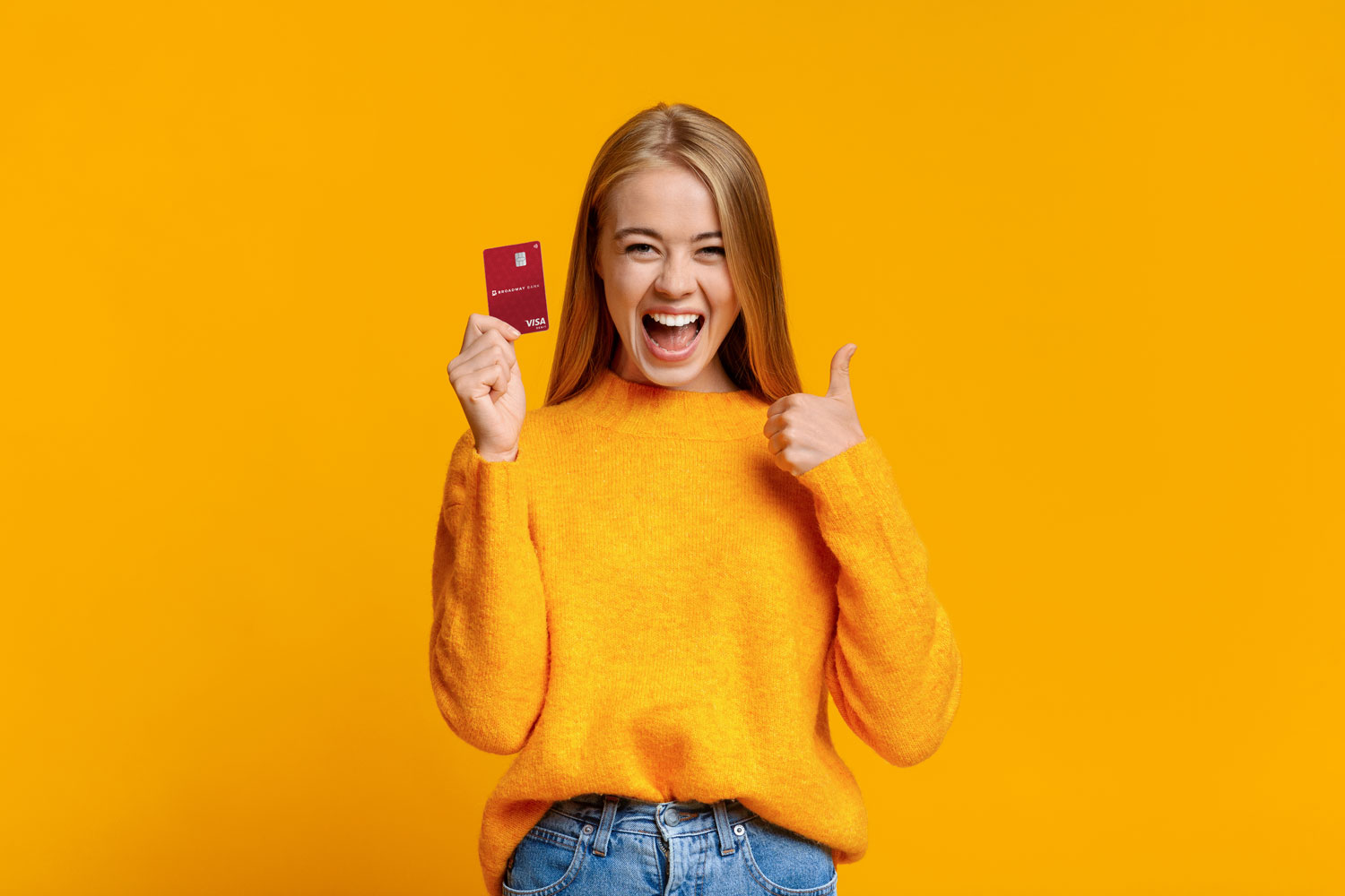 Young lady smiling, holding a Broadway Bank debit on a yellow background