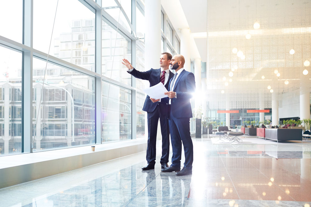 Two men looking looking outside with one man holding papers in his hand