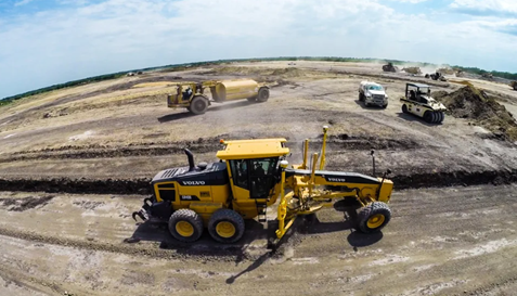 Aerial view of heavy construction machinery, including a Volvo grader and bulldozer, working on a dirt site.