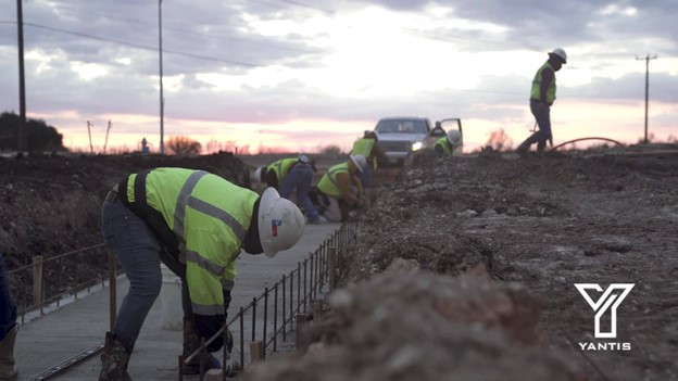 Construction workers in reflective gear pour concrete at a construction site during sunset.