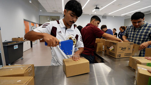 A volunteer seals cardboard boxes using packaging tape during a community service event.
