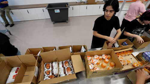 A group of volunteers sorts food into boxes for distribution at a community food program.
