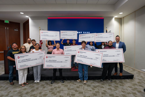 Group of award recipients holding large checks in a bank setting, celebrating their achievements.