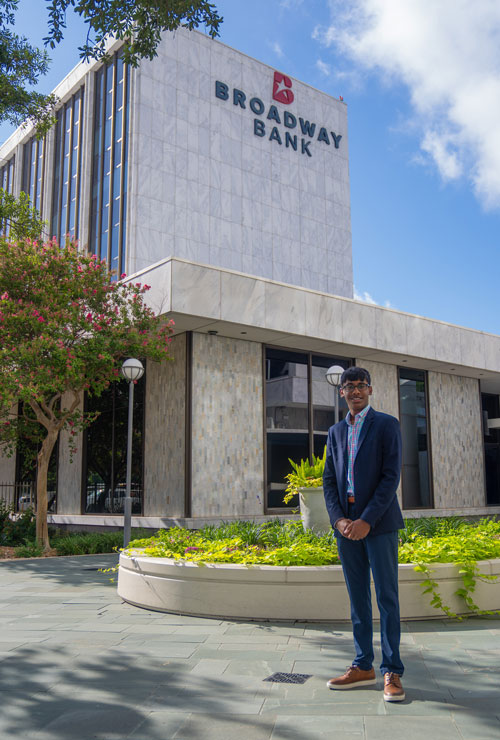 A young professional stands in front of the Broadway Bank building, showcasing modern architecture and landscaped greenery.