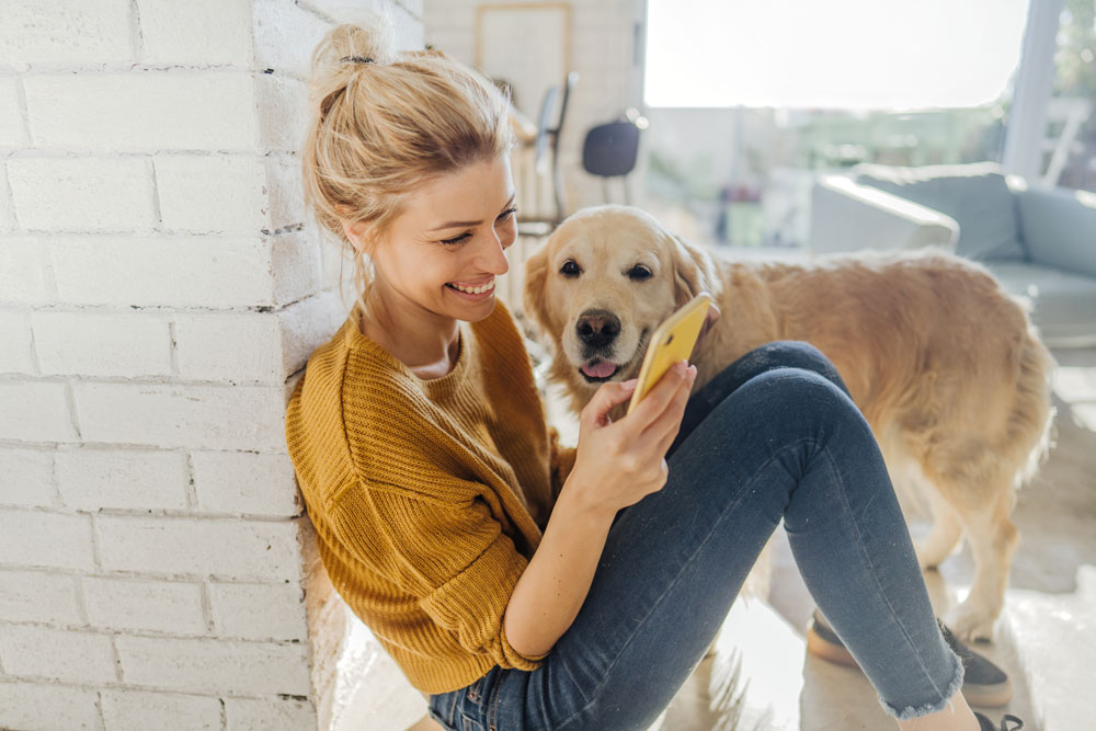 woman sitting on the floor looking at her phone with a dog